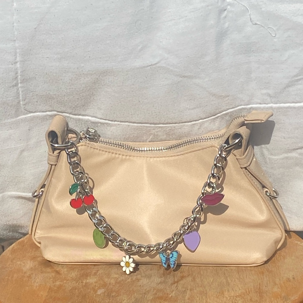 Small Madden NYC oatmilk bag with a silver zipper and charms